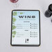 A Wine Country themed menu with a grapevine design on a table with a glass of wine.