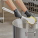 A pair of gloved hands cleaning a stainless steel pot with a Lavex yellow floating utility brush.