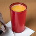 A red Cambro plastic tumbler filled with yellow liquid on a table.
