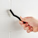 A person using a Lavex toothbrush style grout brush to clean a white tile wall.