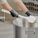 A person wearing black gloves cleaning a large pot with a white Lavex floating utility scrub brush.