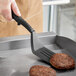 A person using a Fourt&#233; black high heat nylon slotted turner to cook burgers on a pan.