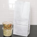 A Duro white paper bag next to a plastic container of pasta and vegetables.