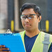 A man wearing Honeywell Uvex safety reader glasses and a safety vest holding a clipboard.