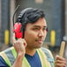 A man wearing Howard Leight by Honeywell red over-the-head digital AM/FM earmuffs and a yellow safety vest while using a hammer.