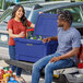 A man and woman sitting in the back of a truck with a CaterGator navy cooler.
