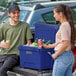 A man and woman standing next to a CaterGator outdoor cooler holding cans of soda.