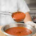 A person using a Vollrath Ivory Solid Round Spoodle to serve red sauce.