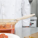 A person in a white coat using a Vollrath ivory round spoodle to serve food from a container.