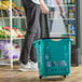 A person pushing a Regency Green shopping basket with wheels.