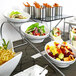 A stainless steel bowl holder with 3 slanted compartments holding food bowls on a buffet table.