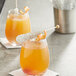 Two glasses of orange juice with Roses Dryden and Palmer silver wrapped rock candy swizzle sticks on top.