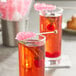 A glass of pink liquid garnished with a Roses Dryden and Palmer pink cherry rock candy swizzle stick.