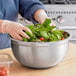 A person in gloves mixes a salad in a large stainless steel mixing bowl with a silicone bottom.