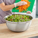 A woman using a Choice stainless steel mixing bowl to cut salad over a bowl of greens and tomatoes.
