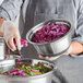 A woman in a chef's uniform holding a bowl of shredded red cabbage in a Choice stainless steel mixing bowl with a silicone bottom.