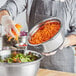 A person holding a Choice stainless steel mixing bowl filled with shredded carrots.