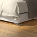 A bed with white bedding stabilized with Wobble Wedges on a wooden floor.