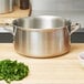 A Vollrath stainless steel sauce pot on a wood surface with parsley.