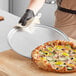 A person using a Choice 15" Aluminum Wide Rim Pizza Pan to clean a pizza.