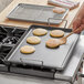 A person using a Vigor portable aluminum griddle to cook a pancake.