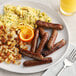 A plate of breakfast food with sausages, eggs, and oranges.