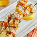 A skewer of Regal Greek Seasoned chicken and vegetables on a white plate with a lemon wedge.