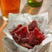 A basket of meat in paper with a glass of beer.