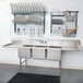 A Regency stainless steel 3 compartment sink with 2 drainboards and racks for utensils.