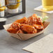 A Bagcraft Packaging EcoCraft natural kraft paper food tray filled with chicken wings and celery sticks on a table.