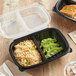 A black plastic container with rice and vegetables in two compartments.