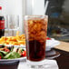 A Libbey stackable beverage glass filled with soda and ice on a table with food.
