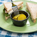 A fork on a plate with a sandwich and pickles with a black fluted ramekin filled with pickles.