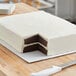 A white cake with two layers cut on a white corrugated half sheet cake board.