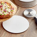 A white pizza circle holding a pizza on a wooden surface.