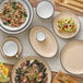 A white stoneware bowl with a black rim filled with pasta and shrimp on a table with other plates and bowls of food.