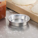 A metal bowl with dough in it next to a round silver metal pizza pan on a counter.