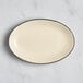 An Acopa cream white stoneware platter with a black rim on an oval shape.