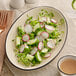 A plate with salad including cucumbers and radishes on a white Acopa stoneware platter.