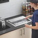 A woman slides a stainless steel lid into a drop-in ice bin on a counter in a professional kitchen.