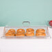 A clear Cambro dome display cover over a tray of bagels on a shelf.
