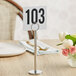 A Tablecraft chrome-plated menu holder with a table number on it on a table with flowers.