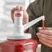 A person using a Heinz plastic condiment pump to pour sauce into a container.