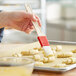 A person using a white and red Choice pastry brush to baste croissants.