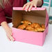 A woman holding a pink bakery box with croissants inside.