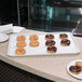 A Carlisle white fiberglass bakery tray holding chocolate covered donuts on a counter.
