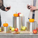 A group of people using Tablecraft stainless steel nesting risers to display wine glasses and apples.