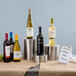 A Tablecraft stainless steel nesting riser set displaying wine bottles on a table.