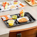 A black Choice right-handed heavy-duty melamine 6 compartment tray with food and drinks in it on a table.