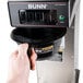 A hand pressing a button on a Bunn commercial pourover coffee maker.